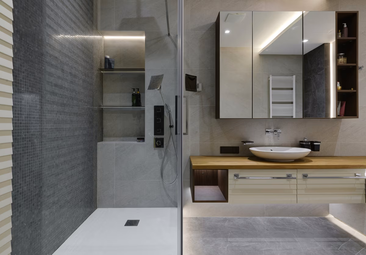Contemporary bathroom featuring textured grey wall, floating wooden vanity, and illuminated mirror cabinet