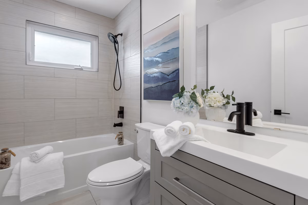 Modern coastal bathroom with grey tile walls, black fixtures, and watercolor artwork
