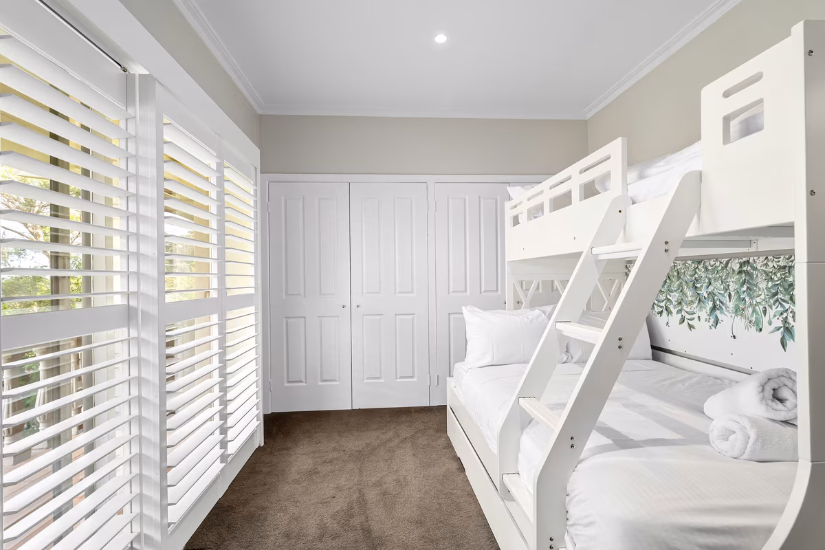 Modern white bunk bed kids room with botanical wall decals and plantation shutters