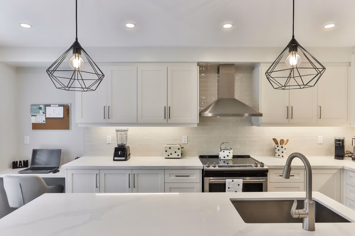 Modern white L-shaped kitchen with geometric pendant lights and sleek finishes