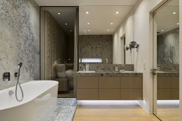 Modern luxury bathroom with textured stone walls, floating illuminated vanity, and freestanding tub