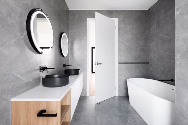 Modern bathroom with grey marble walls, black vessel sinks, and white freestanding tub