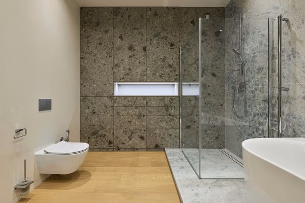 Modern bathroom featuring terrazzo-style walls, wooden flooring, and glass shower enclosure