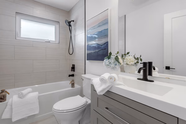 Modern coastal bathroom with grey tile walls, black fixtures, and watercolor artwork