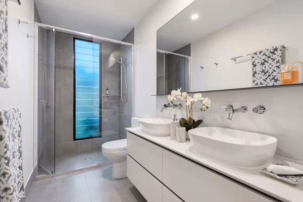 Modern bathroom with blue glass window feature, white vessel sinks, and grey tile accents