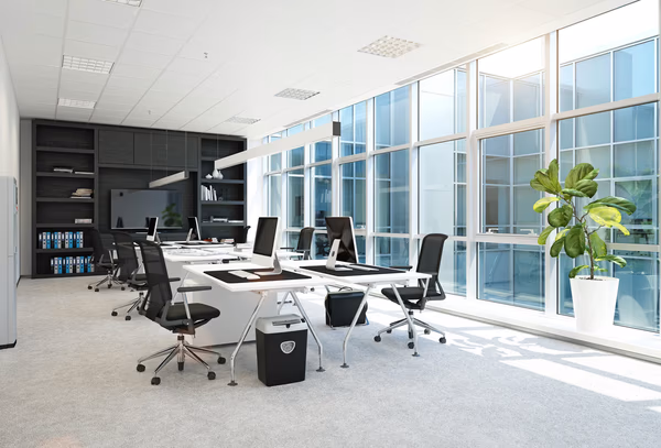 Bright modern office with white desks, ergonomic chairs, and large windows