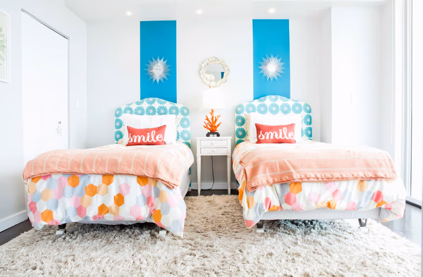 Twin bedroom with turquoise accent walls and coral bedding, featuring decorative sunburst mirrors