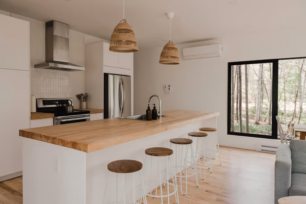 Minimalist white kitchen with wood countertops and rattan pendant lights overlooking garden view