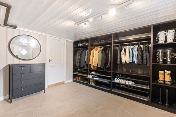 Modern walk-in wardrobe with dark storage units and grey dresser