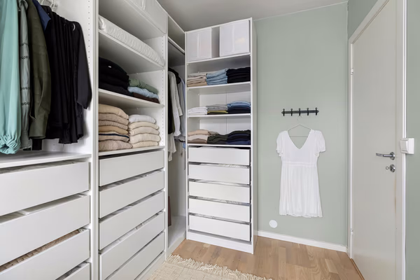 Minimalist white walk-in closet with sage green walls and organized storage systems