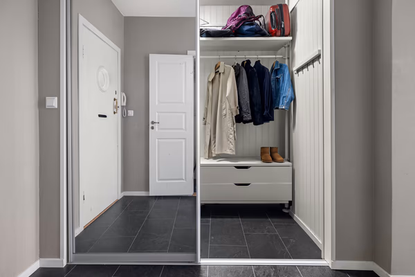 Modern entryway wardrobe with mirrored sliding doors, grey drawers and white paneling